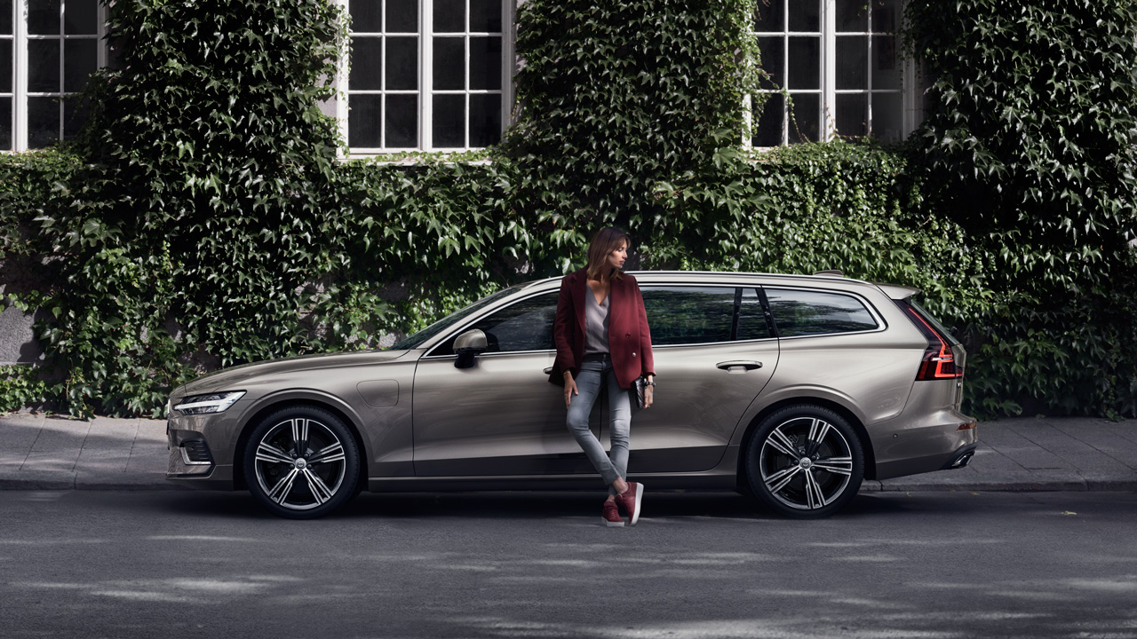 Champagne V90 with woman in front leafy bldg